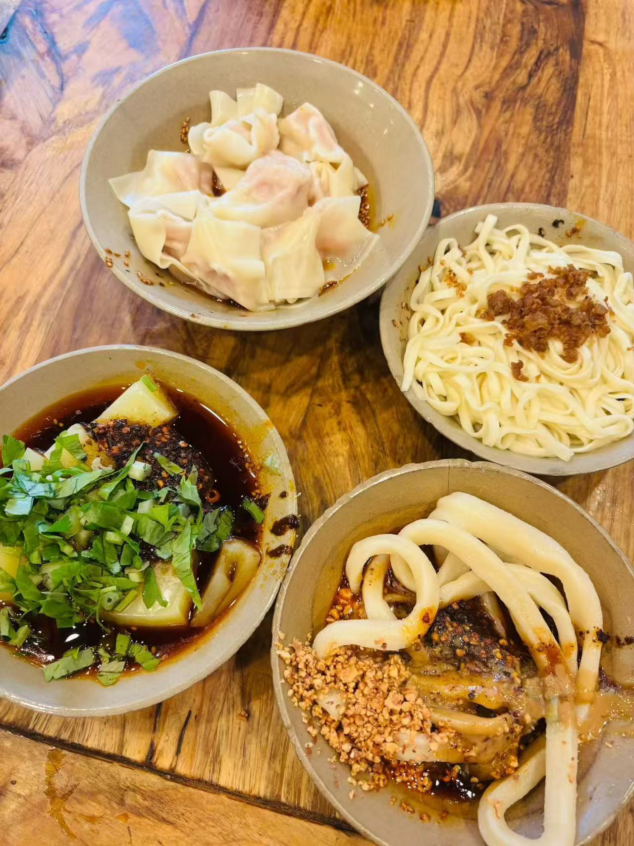 Four bowls of dumplings, noodles and other local dishes on a wooden table.