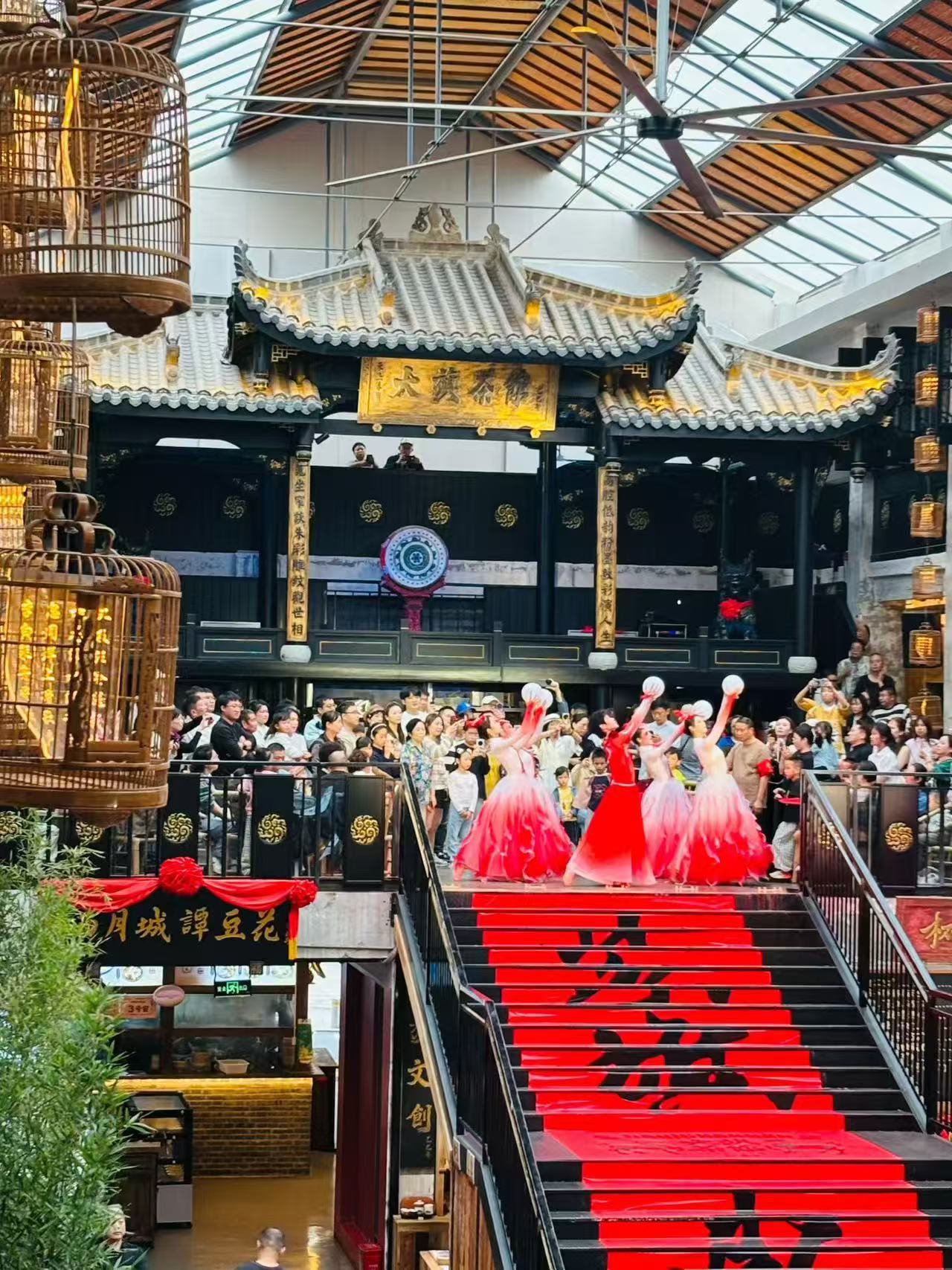 Dancers in pink and red dresses performing above a red staircase as people watch inside a market hall.