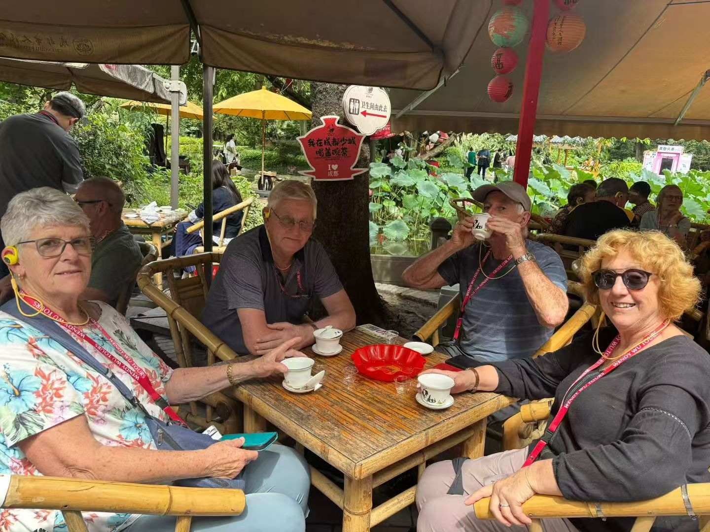 Four guests seated around a wooden tea table under a canopy at an outdoor teahouse.