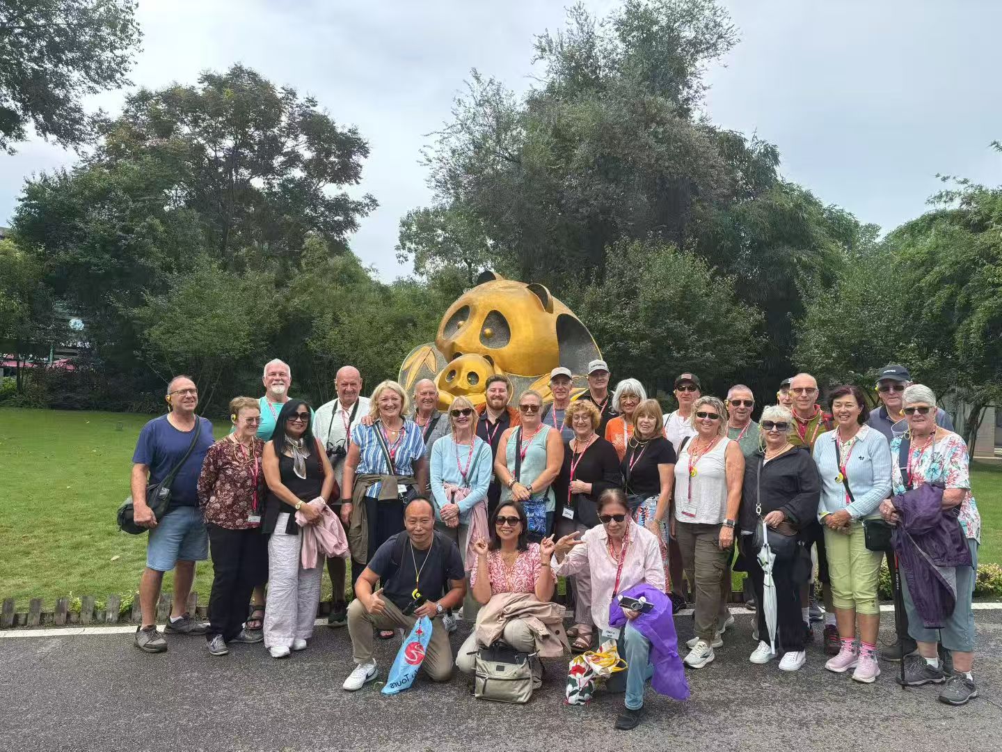 A tour group posing outdoors in front of a golden panda sculpture.