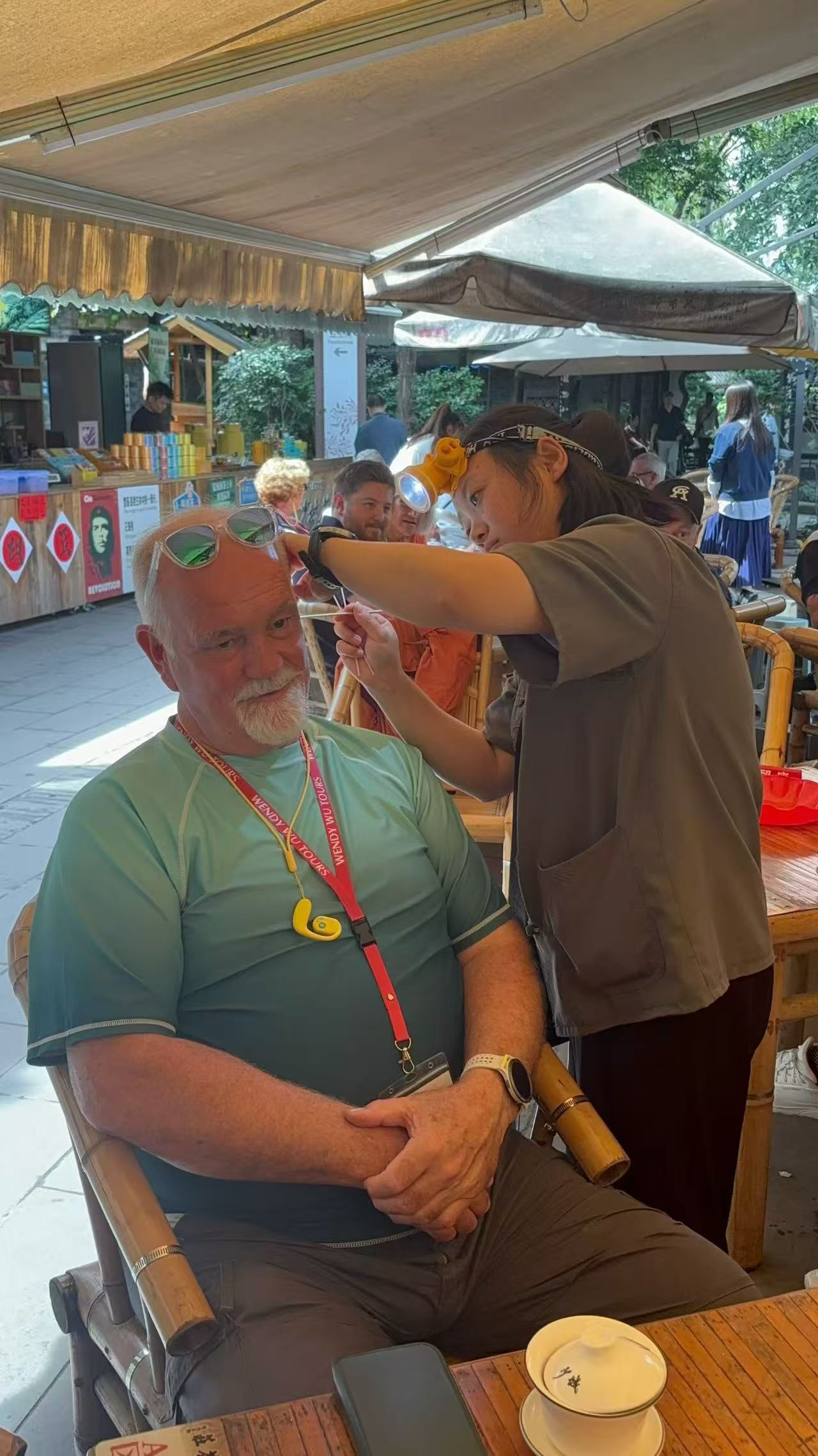 A seated guest receiving an ear-cleaning treatment at an outdoor teahouse.