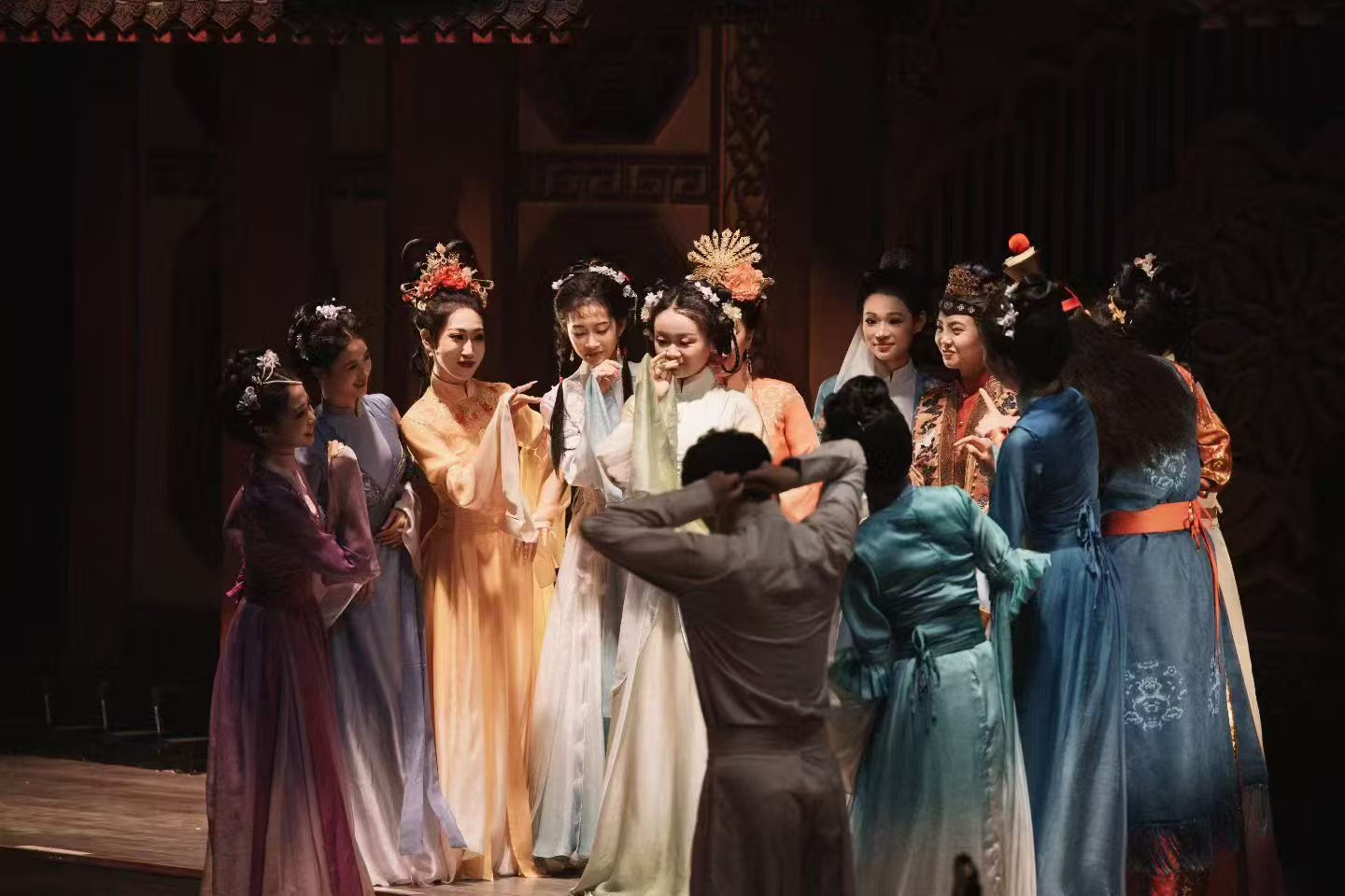 Performers in colourful traditional costumes gathered on stage around a person facing away from the camera.