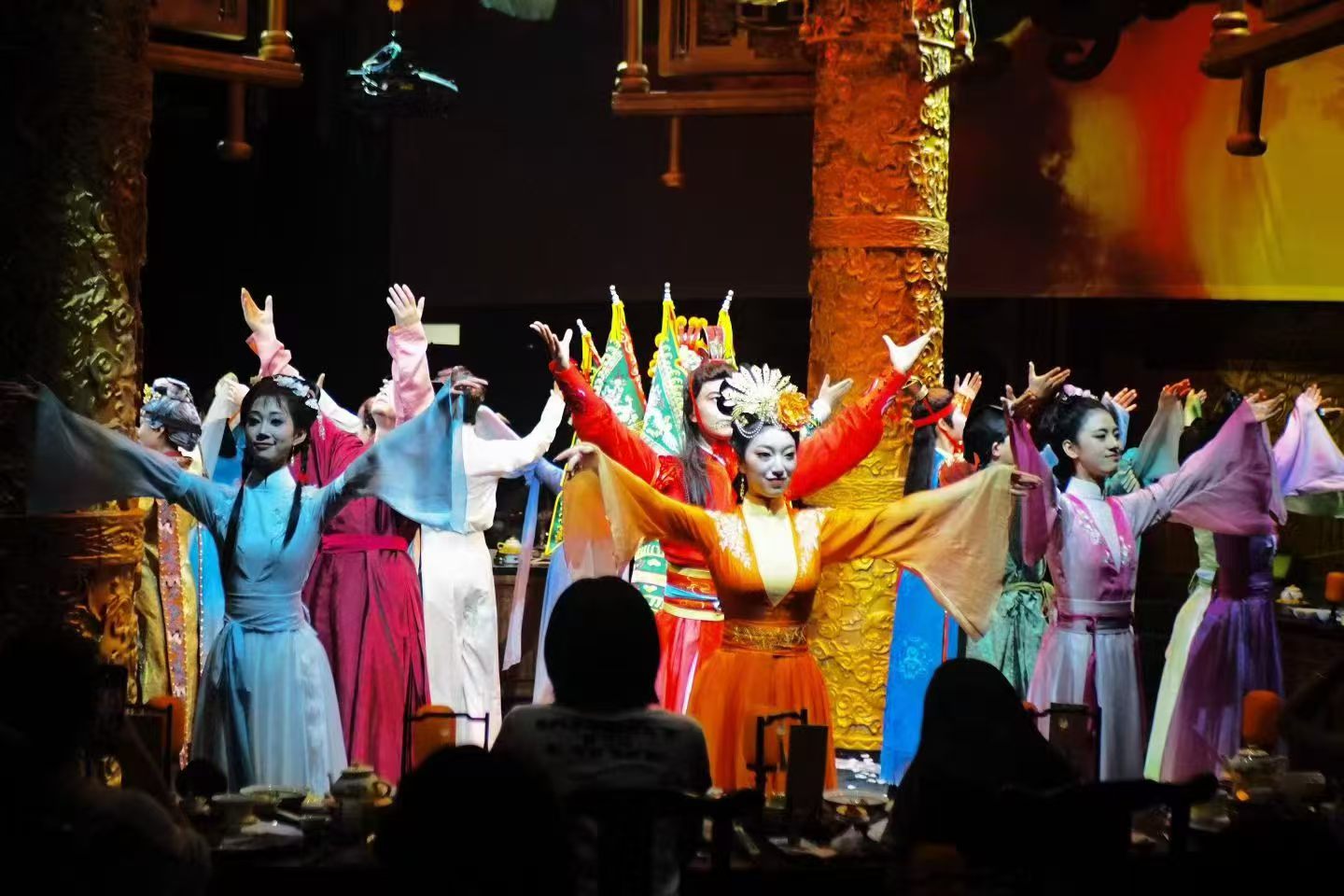 Dancers in flowing blue, orange and purple costumes performing in front of seated diners.