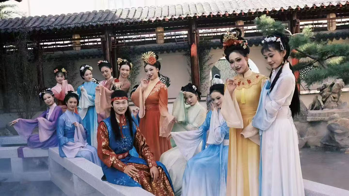 A group in colourful traditional costumes posing beside a stone bridge in a courtyard.