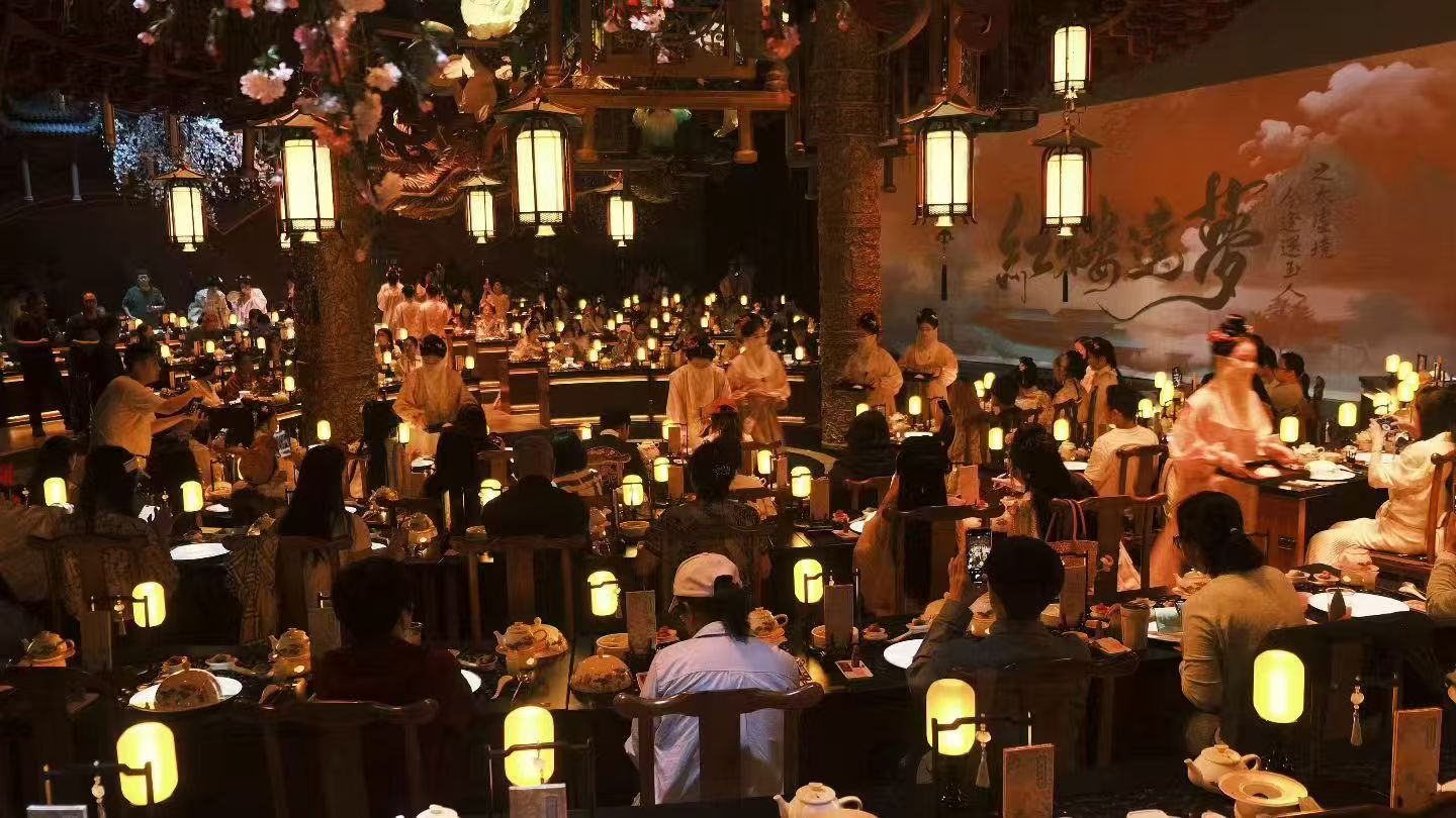 Diners seated beneath lanterns while performers in traditional dress move through the dining hall.