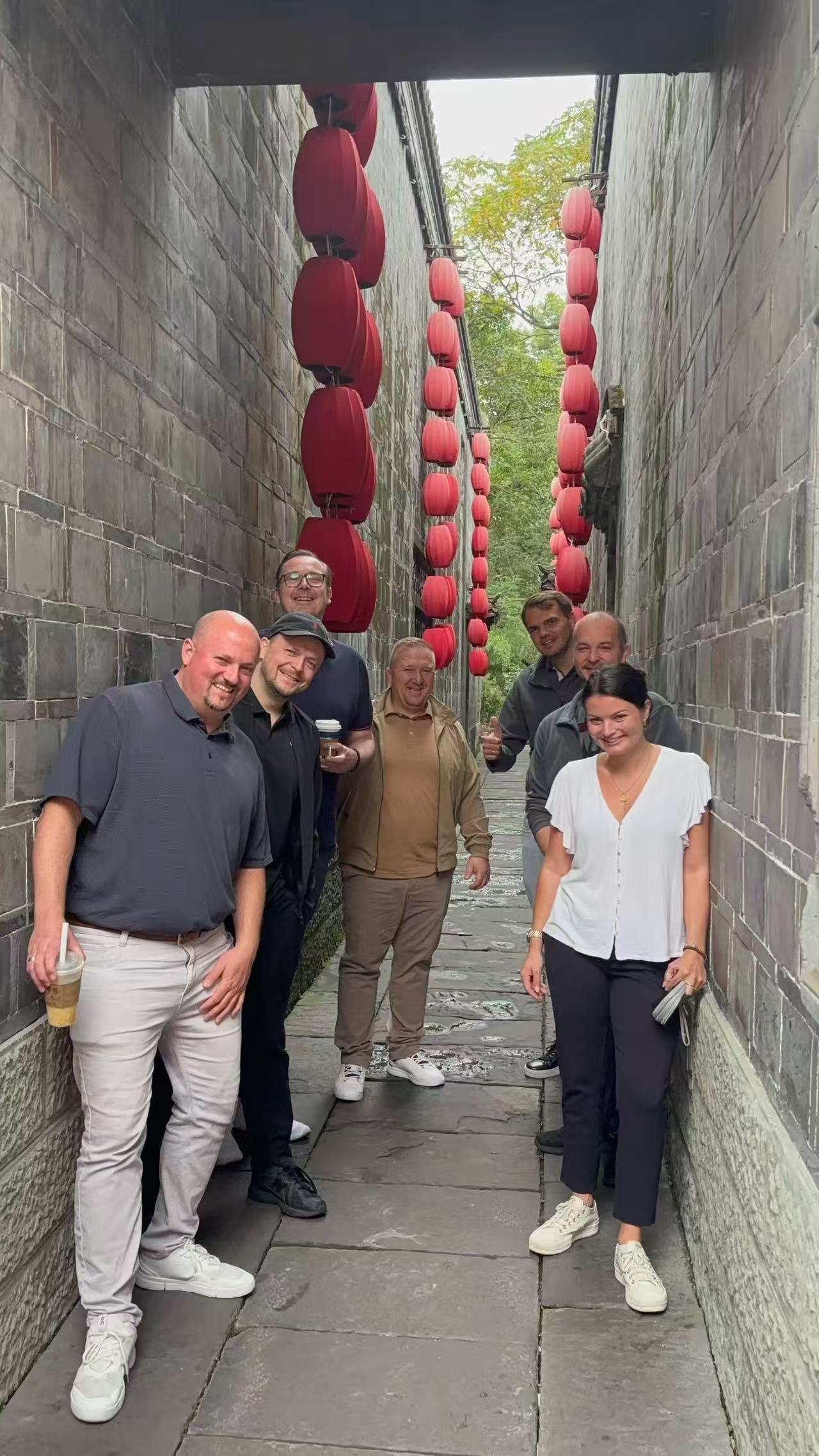 Guests posing in a narrow stone lane beneath rows of red lanterns.