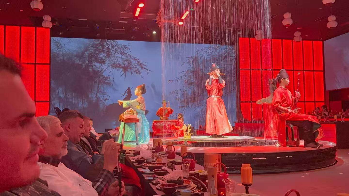 Guests seated beside a circular stage where performers in colourful traditional dress stand under red lights.
