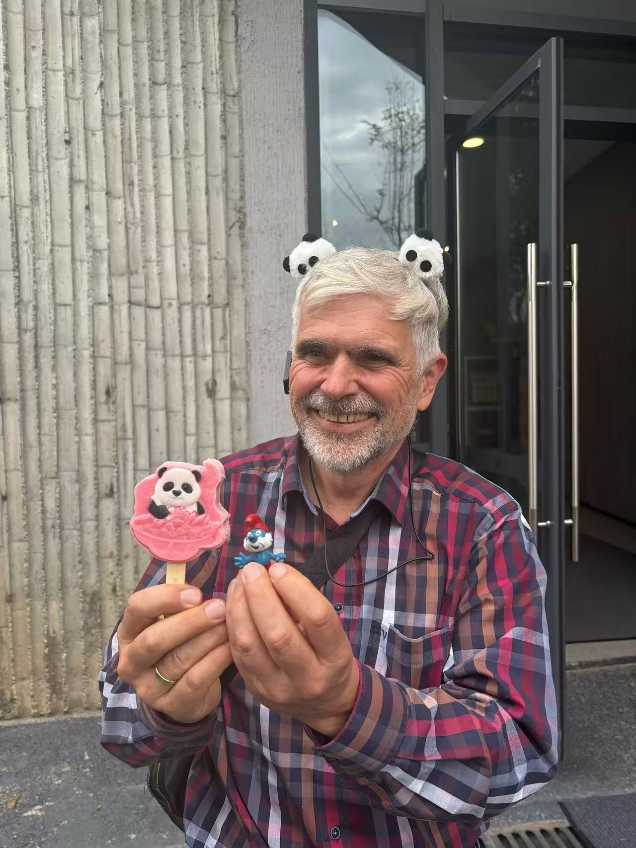 A smiling guest wearing a panda headband and holding a pink panda-shaped treat and a small panda souvenir.
