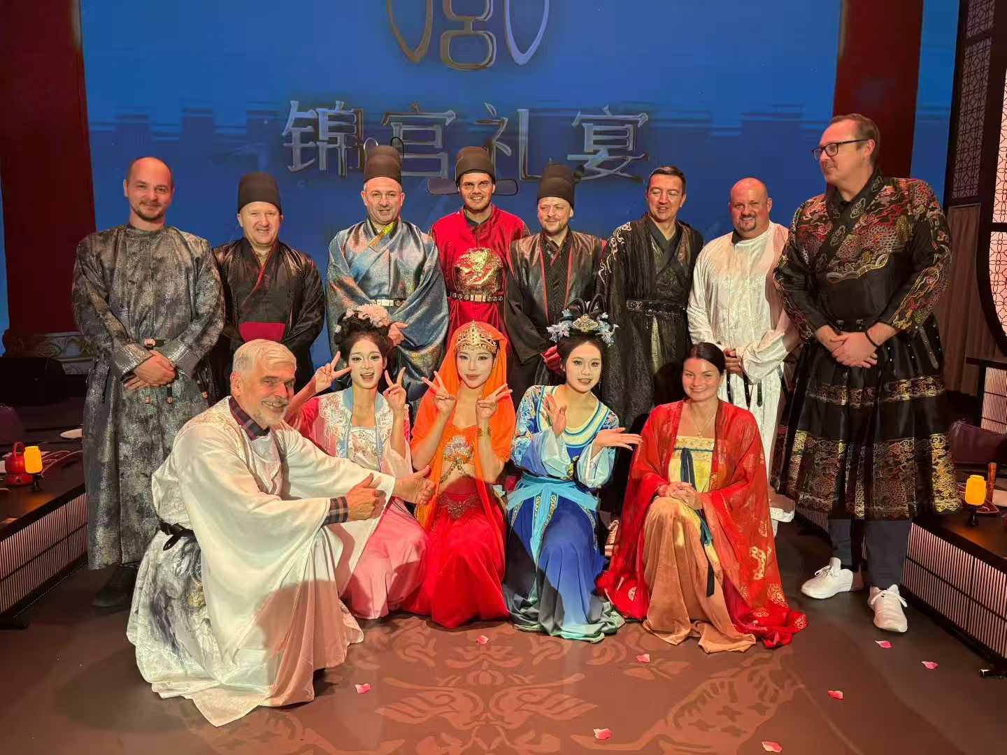 Guests and performers posing together in embroidered robes and colourful traditional costumes.
