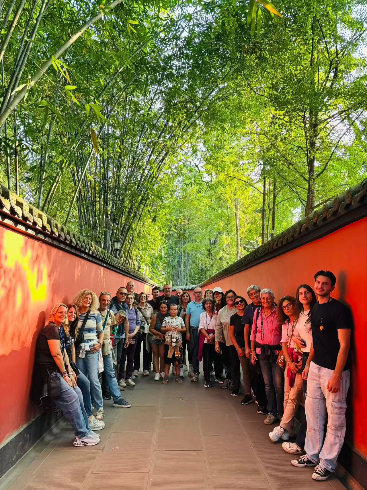 Guests standing along both sides of a stone path between red walls beneath tall green bamboo.